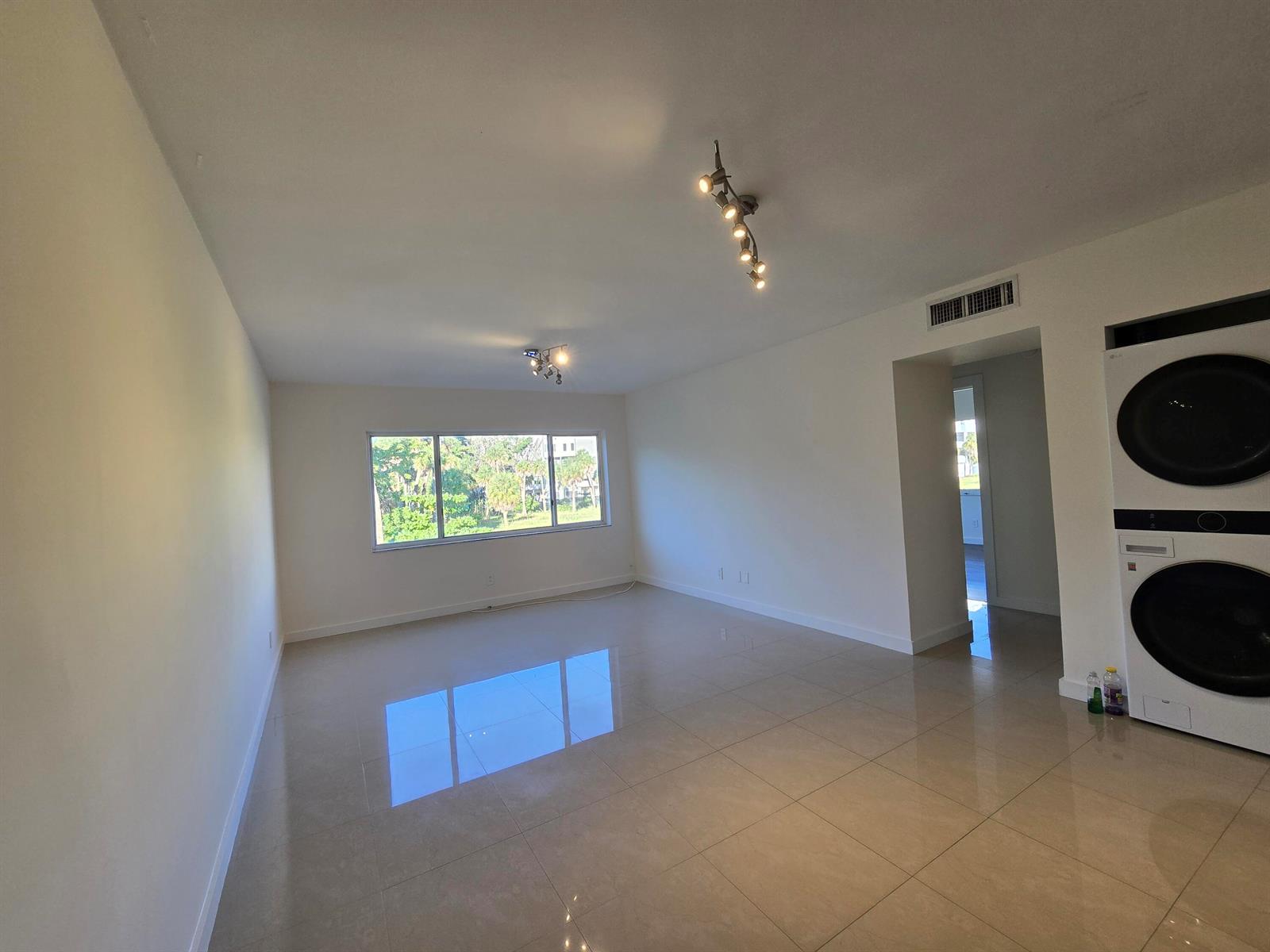 An empty room with light tile flooring, white walls, two track lights, and stacked laundry machines — 201 SE 6th Avenue # 16, Pompano Beach FL 33060, POMPANO BEACH, FL