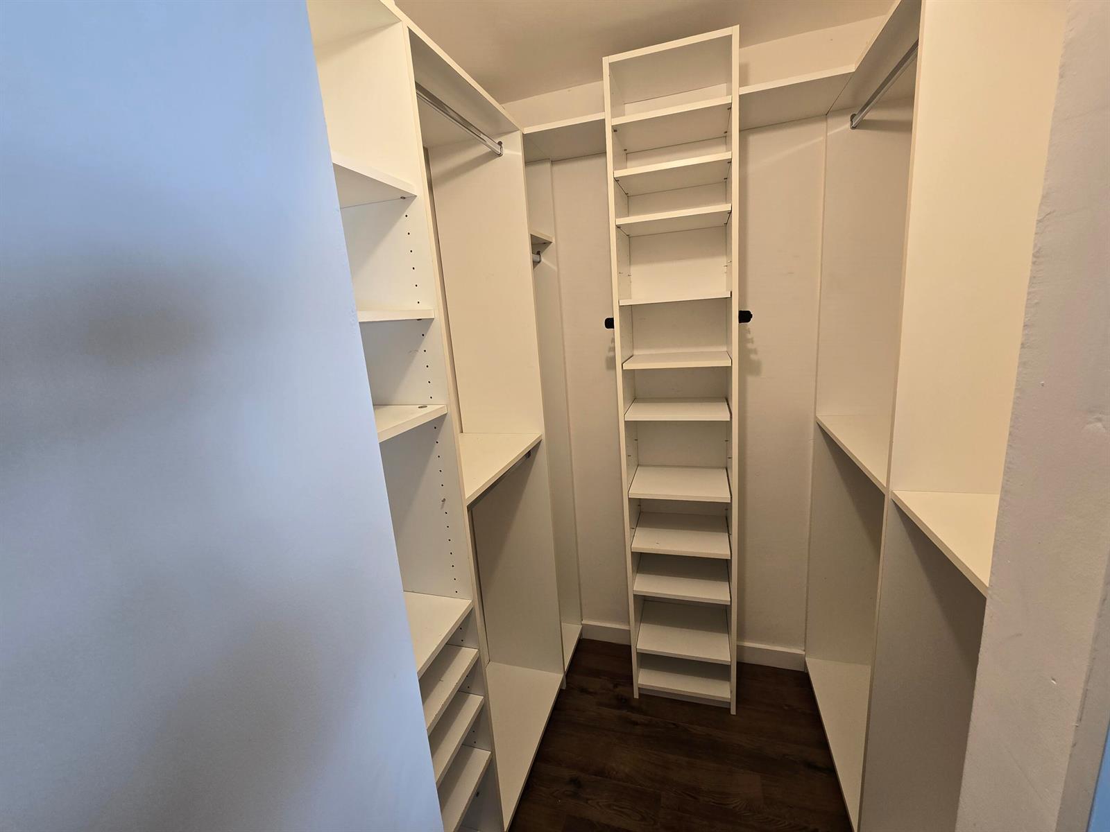 A walk-in closet features white shelving units, hanging rods, and dark wood-look flooring — 201 SE 6th Avenue # 16, Pompano Beach FL 33060, POMPANO BEACH, FL