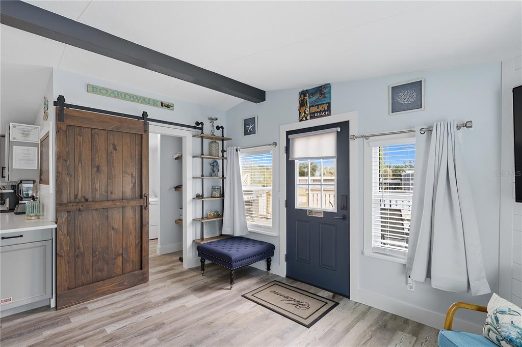 A room with wood-look flooring, a sliding barn door, a blue front door, and shelving — 34 1ST AVENUE, PALM COAST, FL
