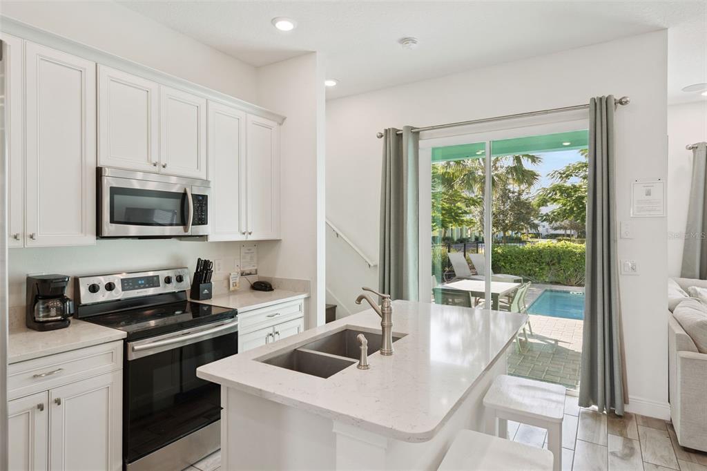 A kitchen with white cabinets, stainless steel appliances, and an island overlooking a backyard pool — 8082 KNEE DEEP ROAD, KISSIMMEE, FL