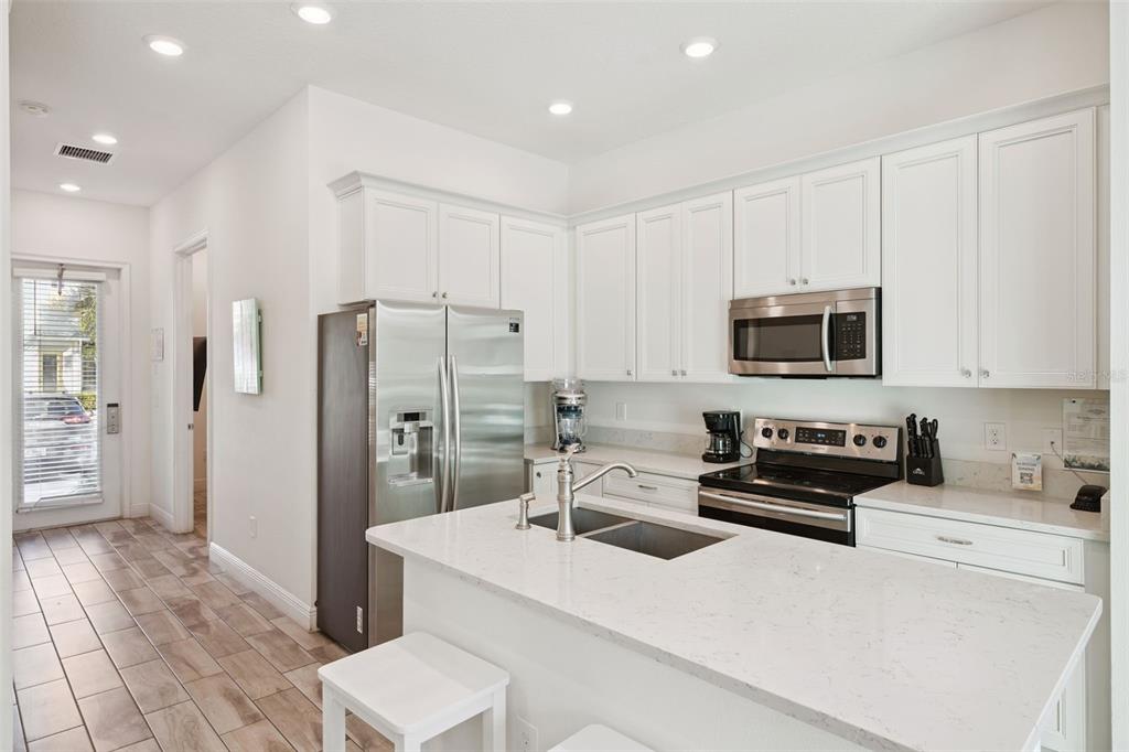 A kitchen features white cabinets, stainless steel appliances, and a quartz-topped island with a sink — 8082 KNEE DEEP ROAD, KISSIMMEE, FL