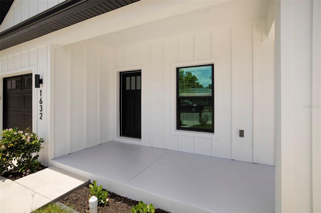 A white board-and-batten exterior features a covered porch, a black front door, and a window — 1632 BALLARD PARK DRIVE, BRADENTON, FL
