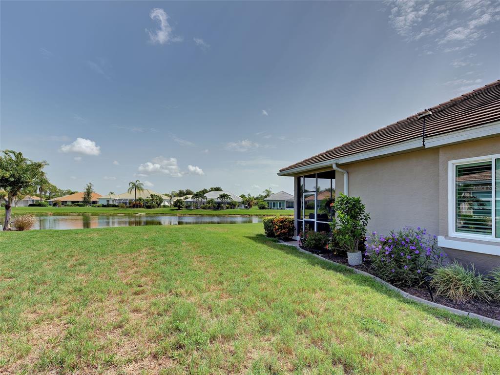 A view of a backyard lawn, a pond, and the side of a house — 5011 SEAGRASS DRIVE, VENICE, FL