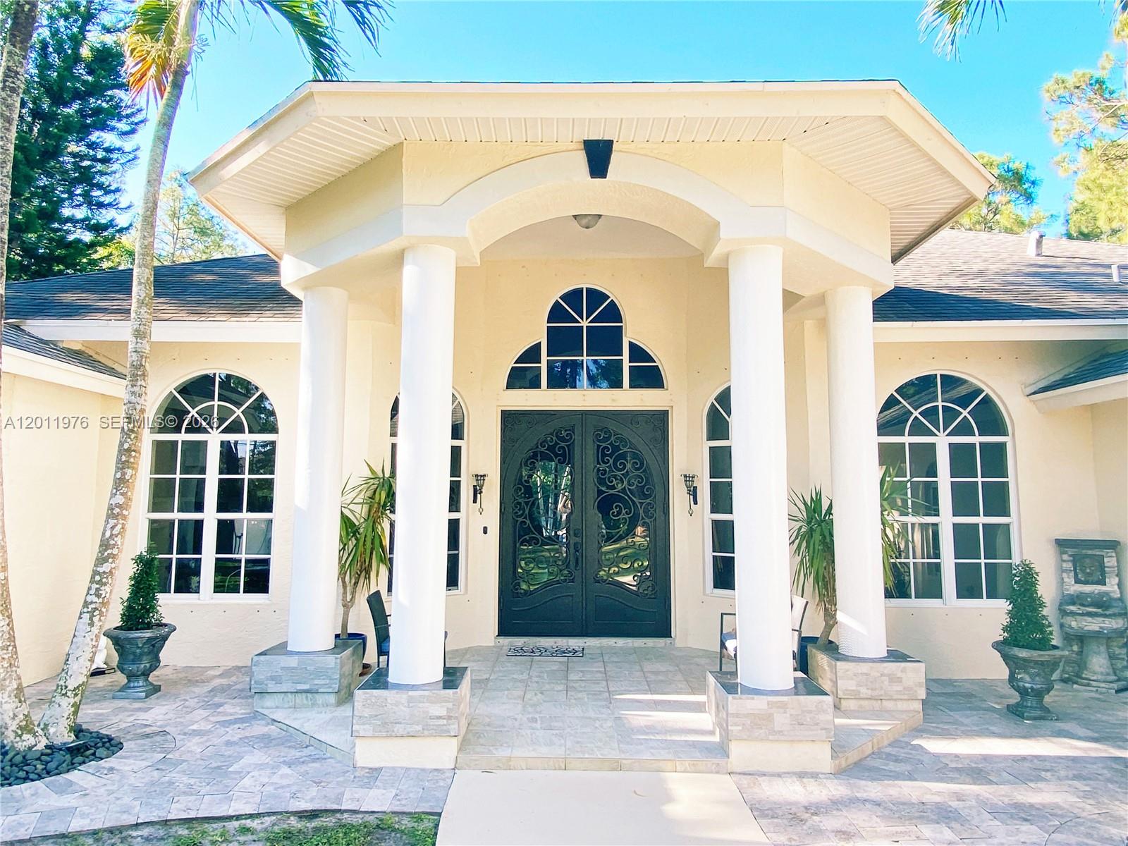 The exterior of a house features a covered entryway with white columns and arched windows — 11576 N 153rd Ct N, Jupiter FL 33478, JUPITER, FL