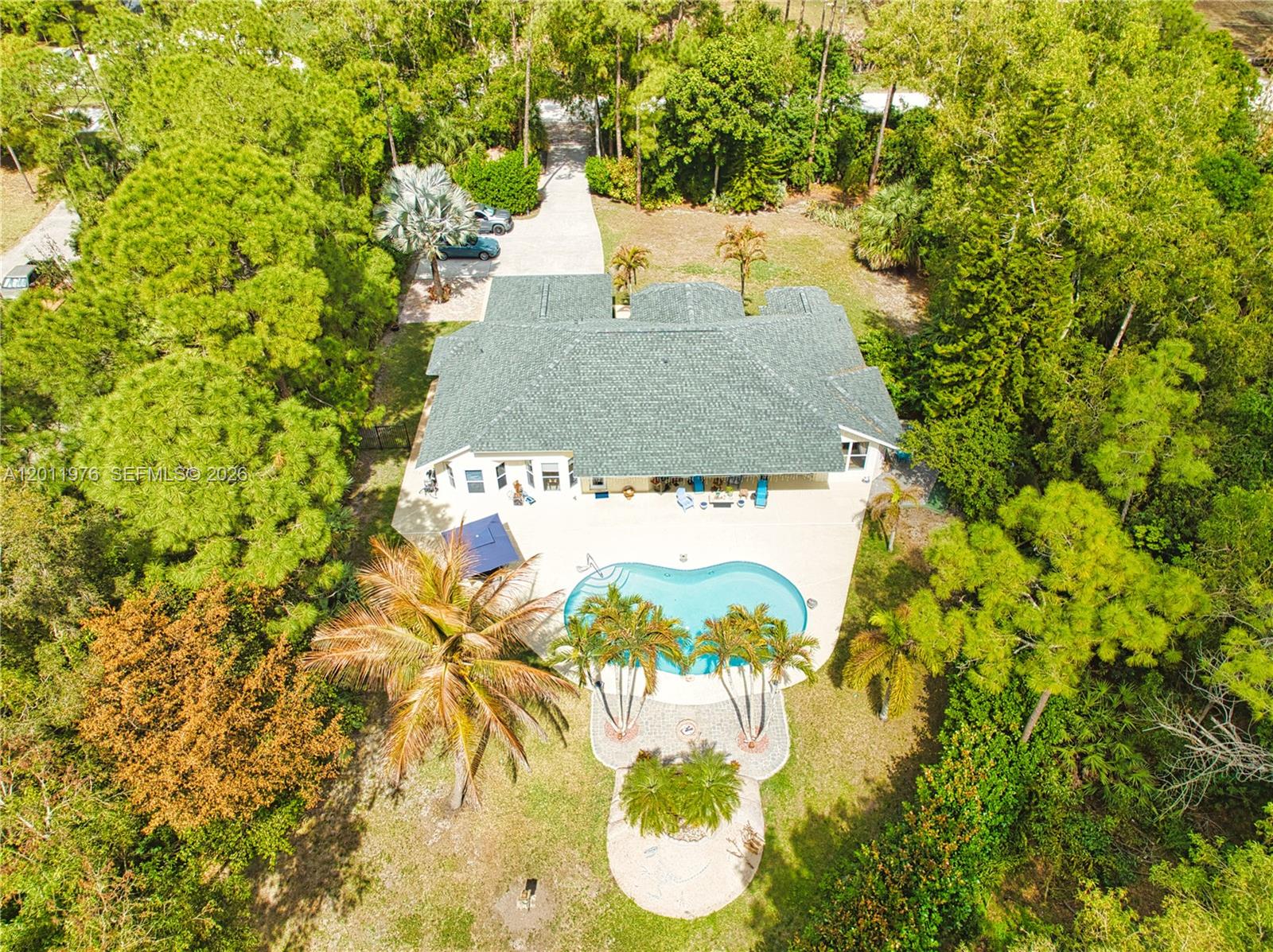 An aerial view shows a house with a pool, patio, and surrounding wooded landscape — 11576 N 153rd Ct N, Jupiter FL 33478, JUPITER, FL