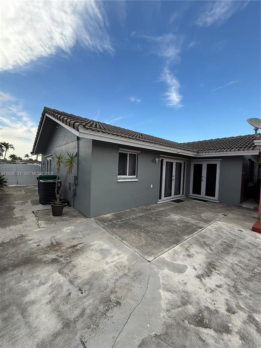 A gray house exterior features a concrete patio, a tiled roof, and glass double doors — 14770 SW 60th St, Miami FL 33193, MIAMI, FL