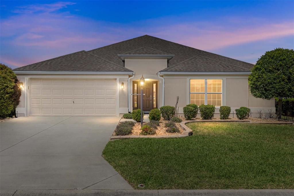 A single-story house with a beige stucco exterior, a two-car garage, and a landscaped yard — 1953 YEARLING WAY, THE VILLAGES, FL