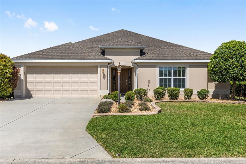 A single-story house with a beige stucco exterior, a two-car garage, and a landscaped yard — 1953 YEARLING WAY, THE VILLAGES, FL