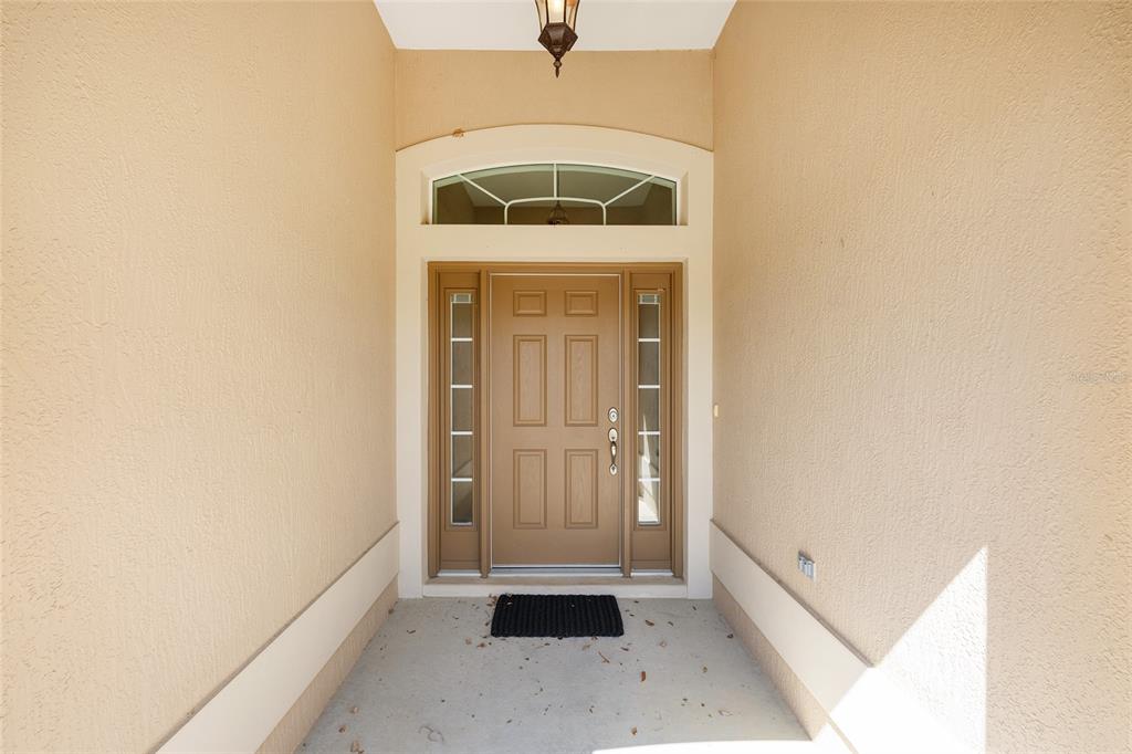 A tan front door with sidelights and an arched transom window sits under a covered entryway — 1953 YEARLING WAY, THE VILLAGES, FL