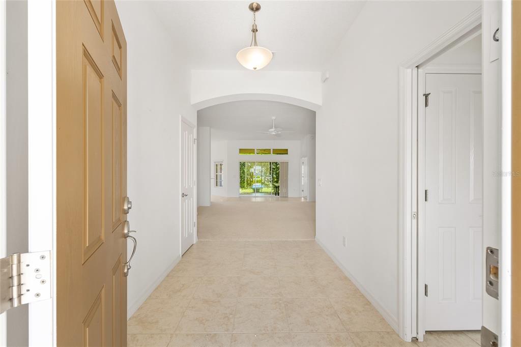 A tiled entryway leads through an arched opening toward a carpeted living area with glass doors — 1953 YEARLING WAY, THE VILLAGES, FL