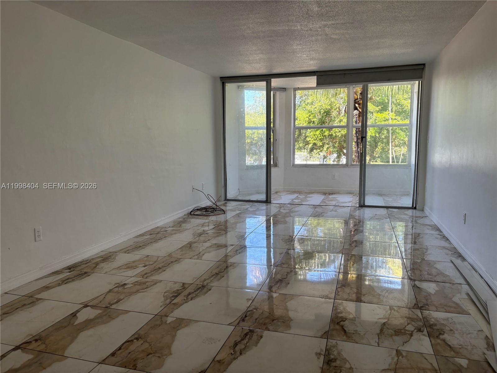 An empty room features white walls, large marble-patterned floor tiles, and sliding glass balcony doors — 1501 NE 191st St # C211, Miami FL 33179, MIAMI, FL