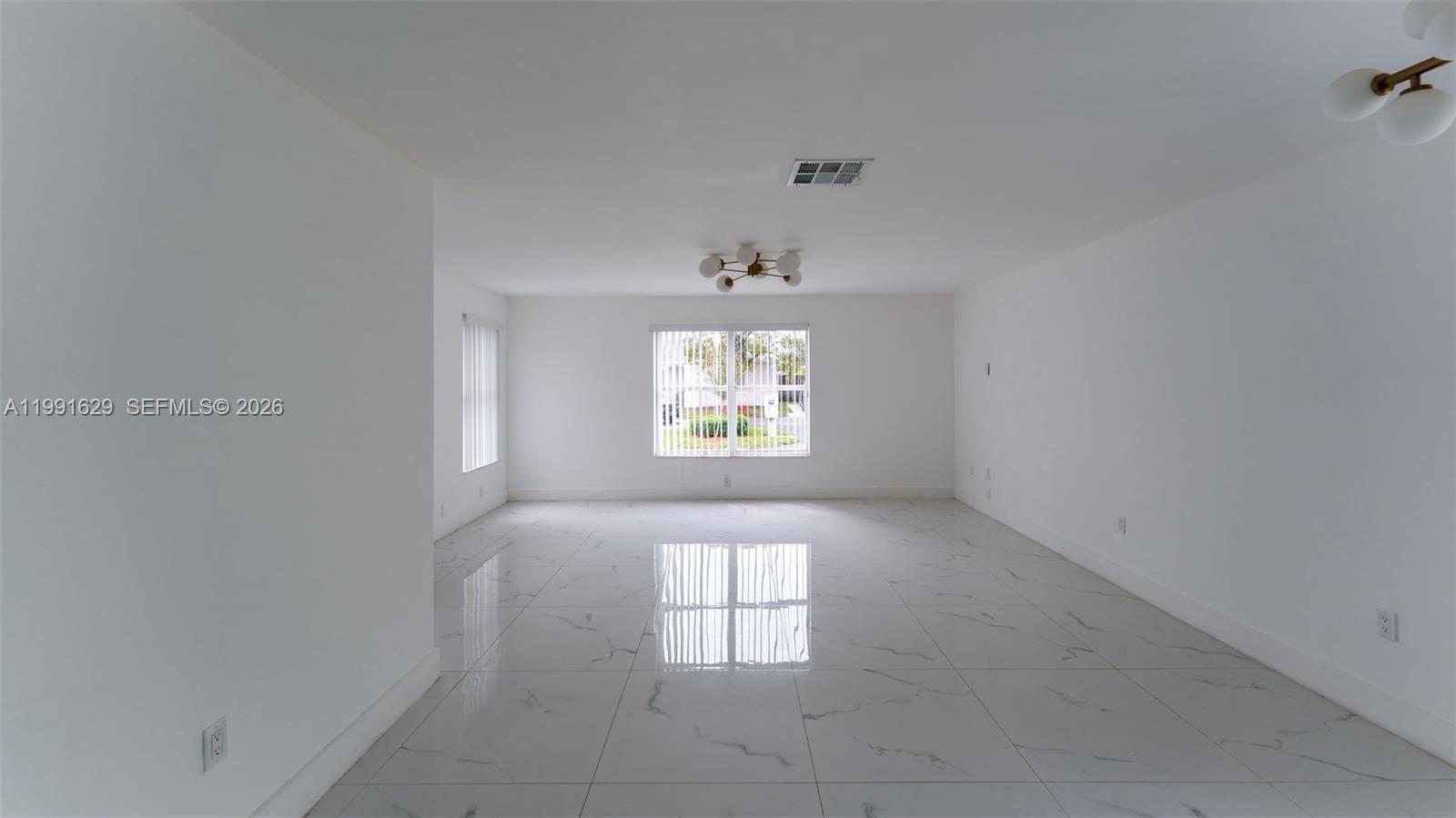 A bright, empty room features white walls, a large window, and polished marble-look tile flooring — 22226 SW 98th Pl, Cutler Bay FL 33190, CUTLER BAY, FL