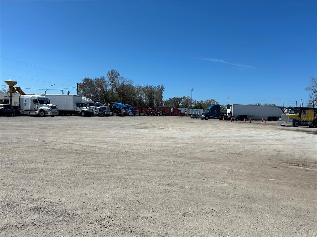 A large, unpaved gravel lot features several parked semi-trucks and trailers under a clear sky — 6910 BENJAMIN ROAD, TAMPA, FL