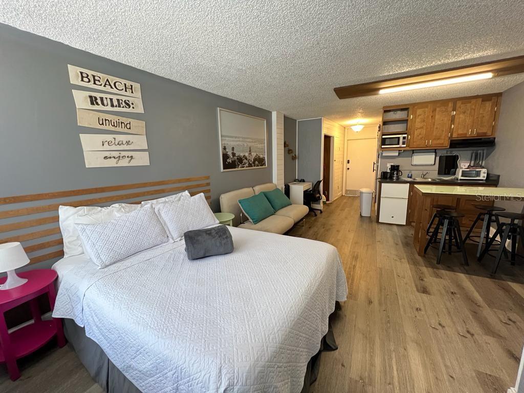 A studio apartment features a bed, a small sofa, and a kitchenette with wooden cabinets — 800 N ATLANTIC AVENUE UNIT 304, DAYTONA BEACH, FL