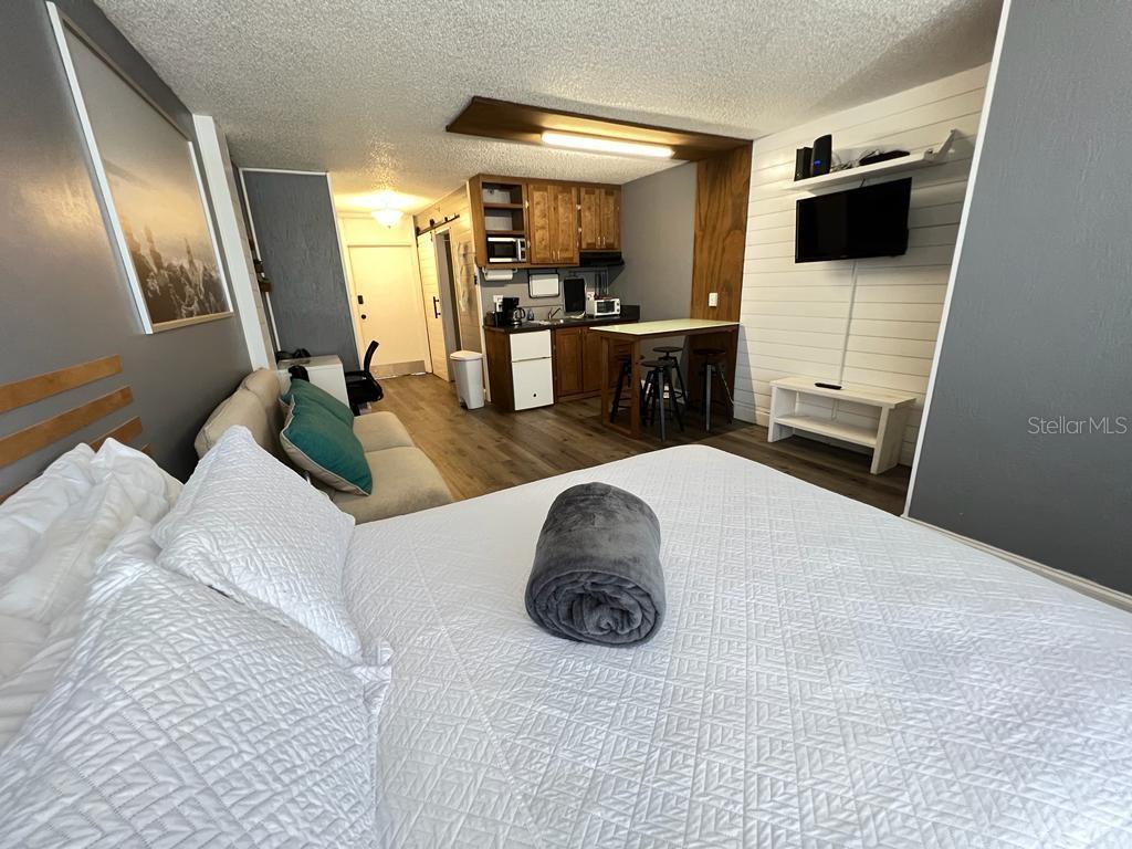 A studio apartment features a bed, a small kitchenette, and a wall-mounted television — 800 N ATLANTIC AVENUE UNIT 304, DAYTONA BEACH, FL