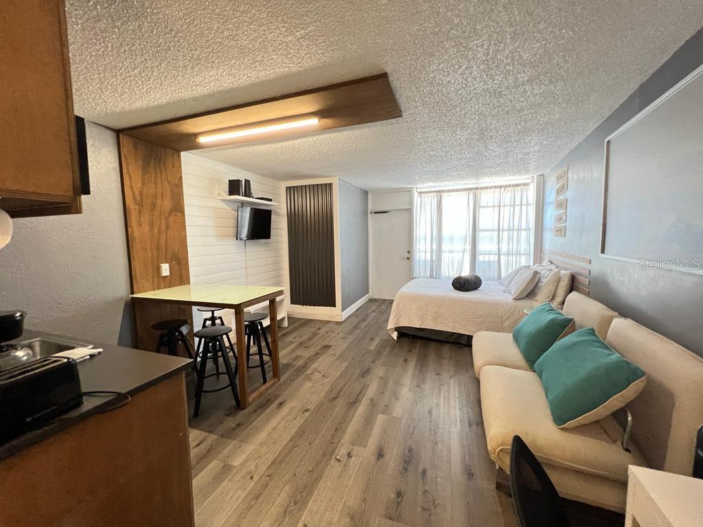 A studio apartment featuring a kitchen, dining area, sofa, and bed with wood-look flooring — 800 N ATLANTIC AVENUE UNIT 304, DAYTONA BEACH, FL