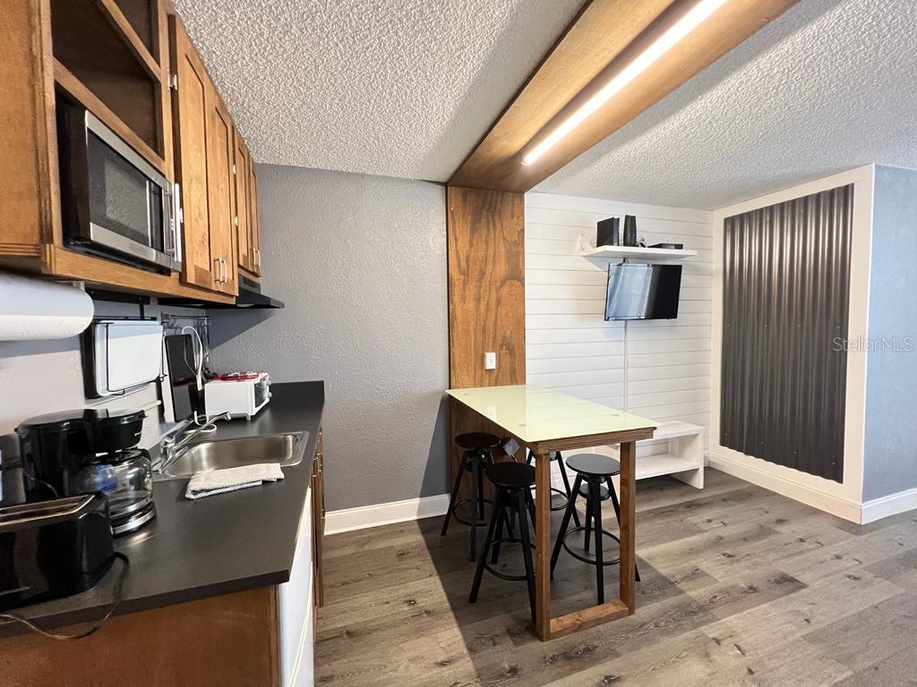 A kitchen features wood cabinets, a glass-topped dining table, and a corrugated metal accent wall — 800 N ATLANTIC AVENUE UNIT 304, DAYTONA BEACH, FL