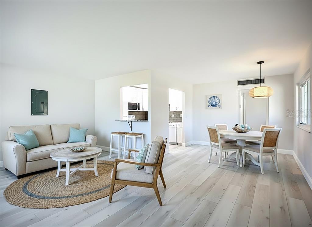A living and dining area with light wood floors, neutral furniture, and a kitchen pass-through — 1811 BEDFORD LANE UNIT 166, SUN CITY CENTER, FL