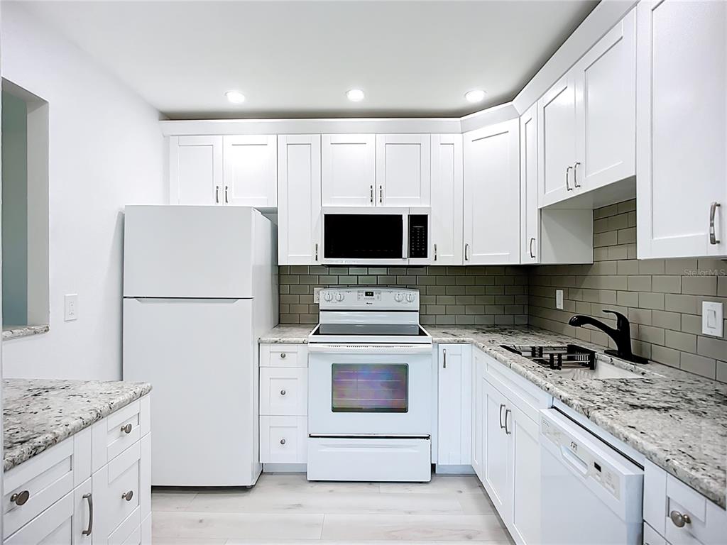 A kitchen features white cabinets, granite countertops, a white stove, and a gray subway tile backsplash — 1811 BEDFORD LANE UNIT 166, SUN CITY CENTER, FL