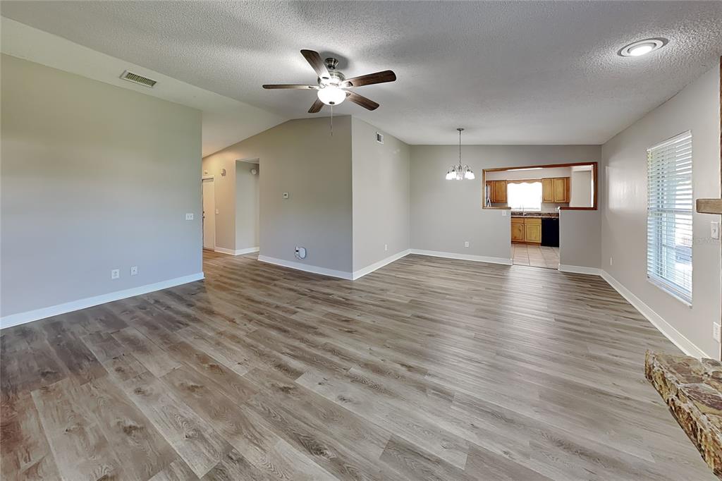 A spacious living area features light wood-look flooring, a ceiling fan, and an open kitchen — 1020 RED OAK CIRCLE, BRANDON, FL