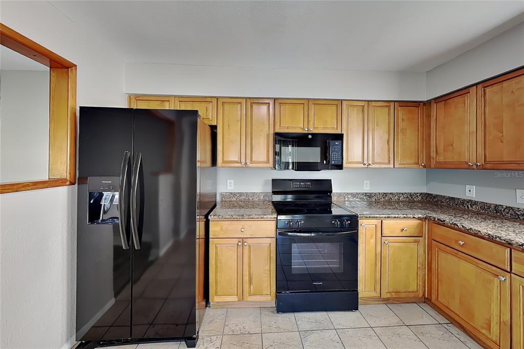 A kitchen features honey-oak cabinets, black appliances, and granite countertops over a tiled floor — 1020 RED OAK CIRCLE, BRANDON, FL