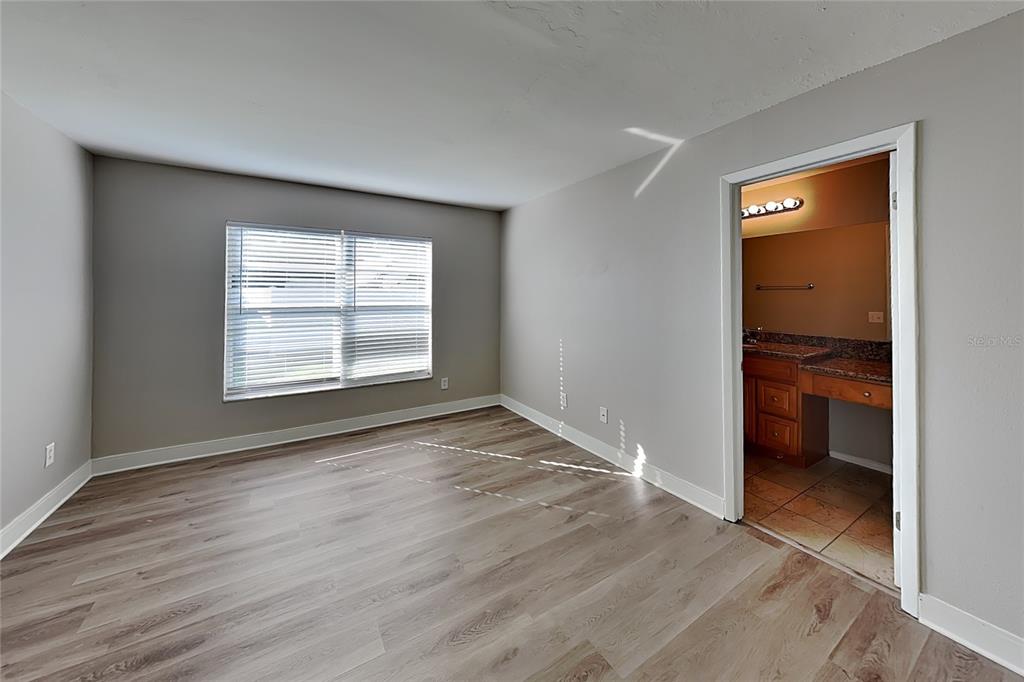 A bedroom with light gray walls, wood-look flooring, and an attached bathroom doorway — 1020 RED OAK CIRCLE, BRANDON, FL