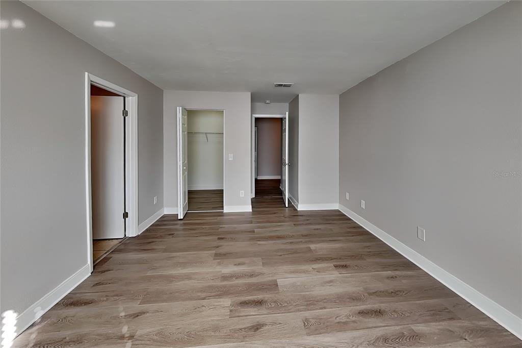 An empty room with gray walls, wood-look flooring, and three open doorways — 1020 RED OAK CIRCLE, BRANDON, FL