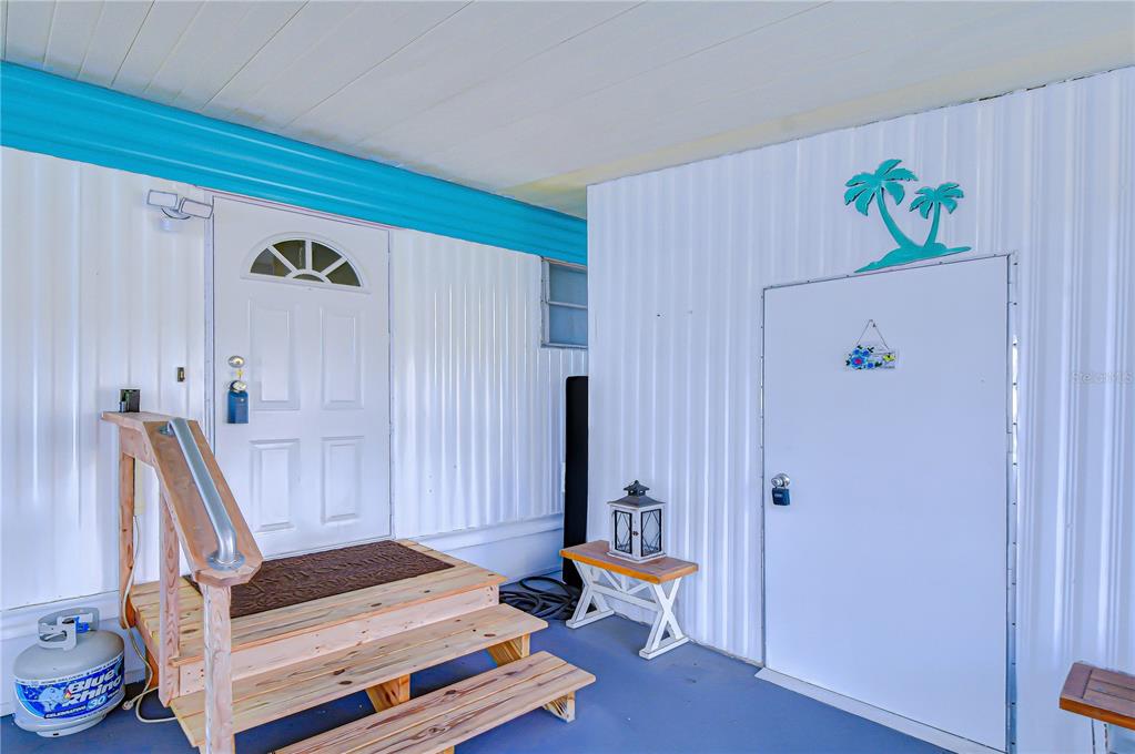 A covered porch features a wooden staircase leading to a white door and metal siding — 38636 REMORA AVENUE, ZEPHYRHILLS, FL