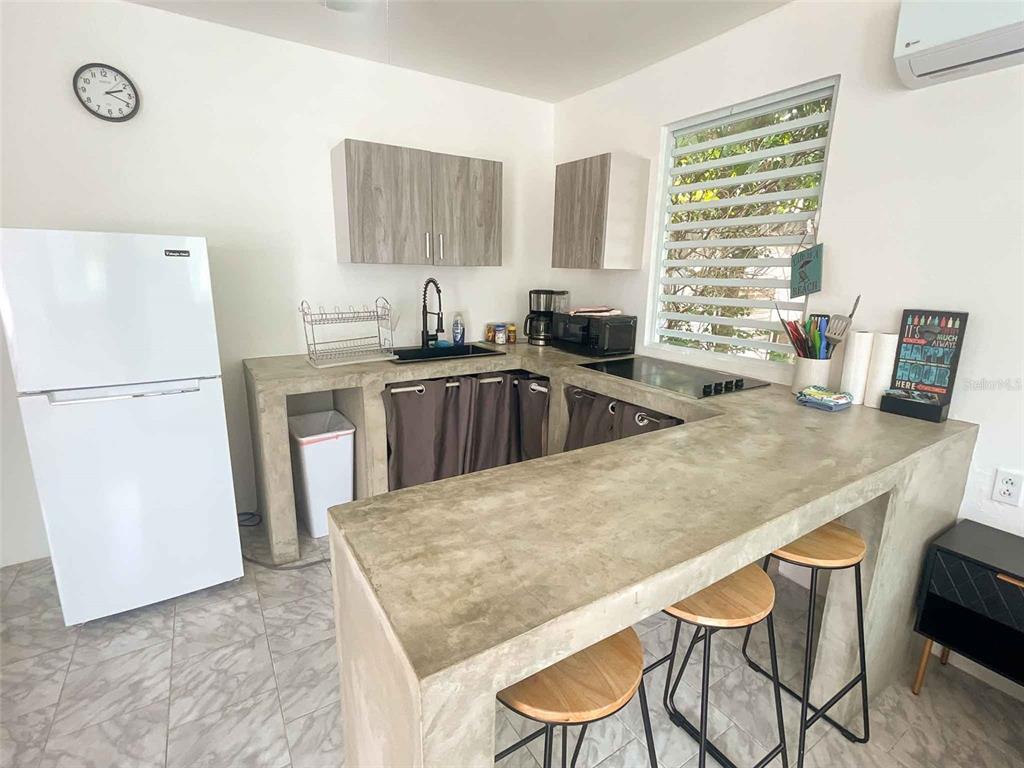 A kitchen features concrete countertops, a white refrigerator, and a breakfast bar with two stools — 376 CALLE GIRASOL, VIEQUES, PR