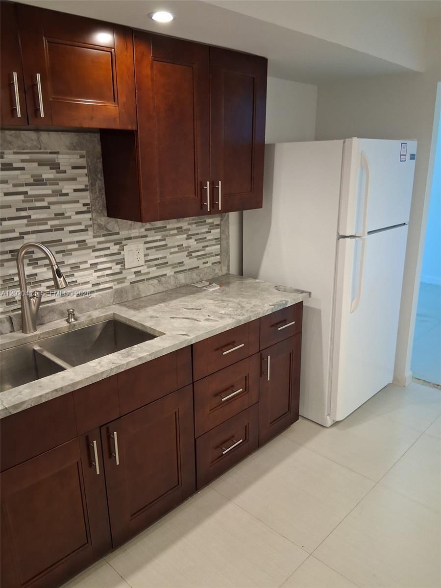 A kitchen features dark wood cabinets, a gray stone-look countertop, and a tiled backsplash — 405 N Ocean Blvd # 1815, Pompano Beach FL 33062, POMPANO BEACH, FL