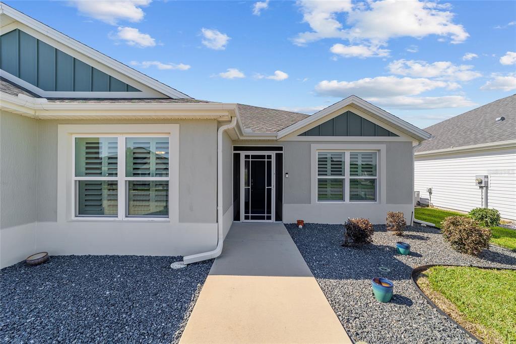 A concrete walkway leads to the front entrance of a single-story house with gray siding — 1106 EBLING LOOP, THE VILLAGES, FL
