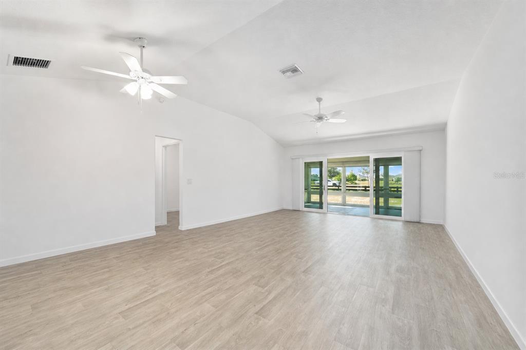 An empty living room with white walls, light wood-look flooring, and two ceiling fans — 1106 EBLING LOOP, THE VILLAGES, FL