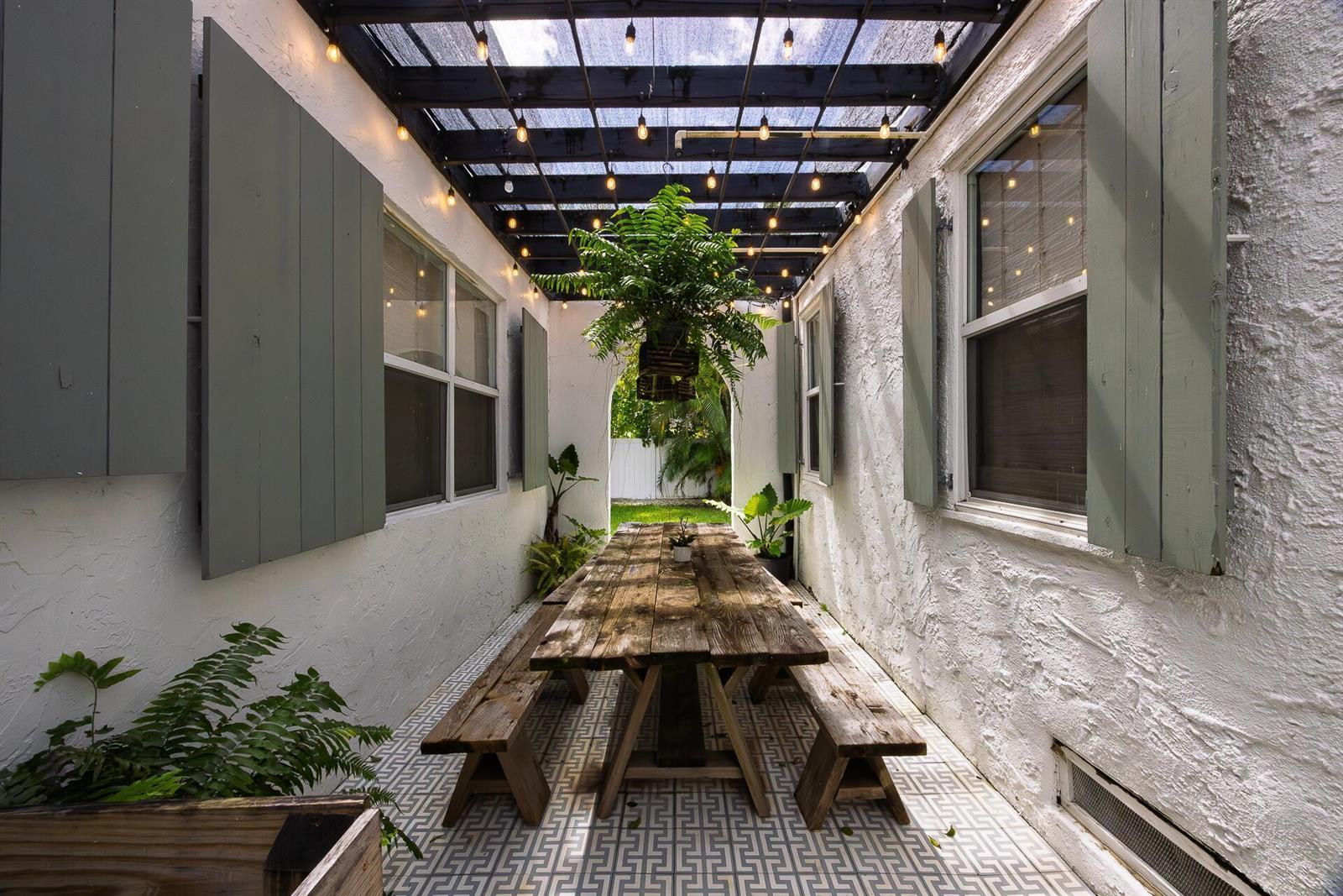A narrow outdoor patio features a wooden picnic table under a pergola with string lights — 717 Forest Hill Boulevard, West Palm Beach FL 33405, WEST PALM BEACH, FL