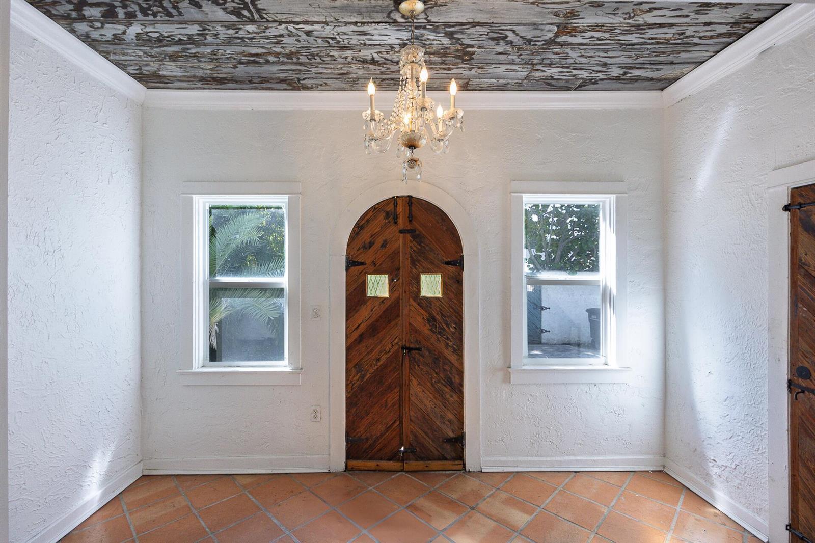 An entryway features a rustic wooden arched door, a crystal chandelier, and a textured ceiling — 717 Forest Hill Boulevard, West Palm Beach FL 33405, WEST PALM BEACH, FL