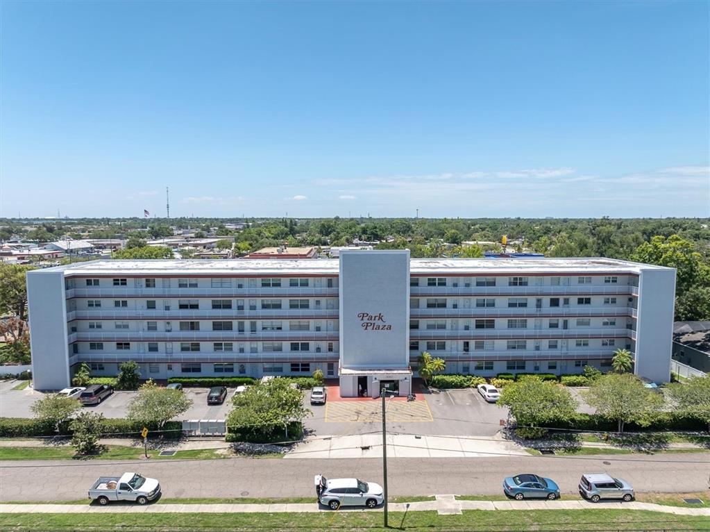 An exterior view of a multi-story apartment building with a central entrance and parking lot — 5060 76TH AVENUE N UNIT 402, PINELLAS PARK, FL