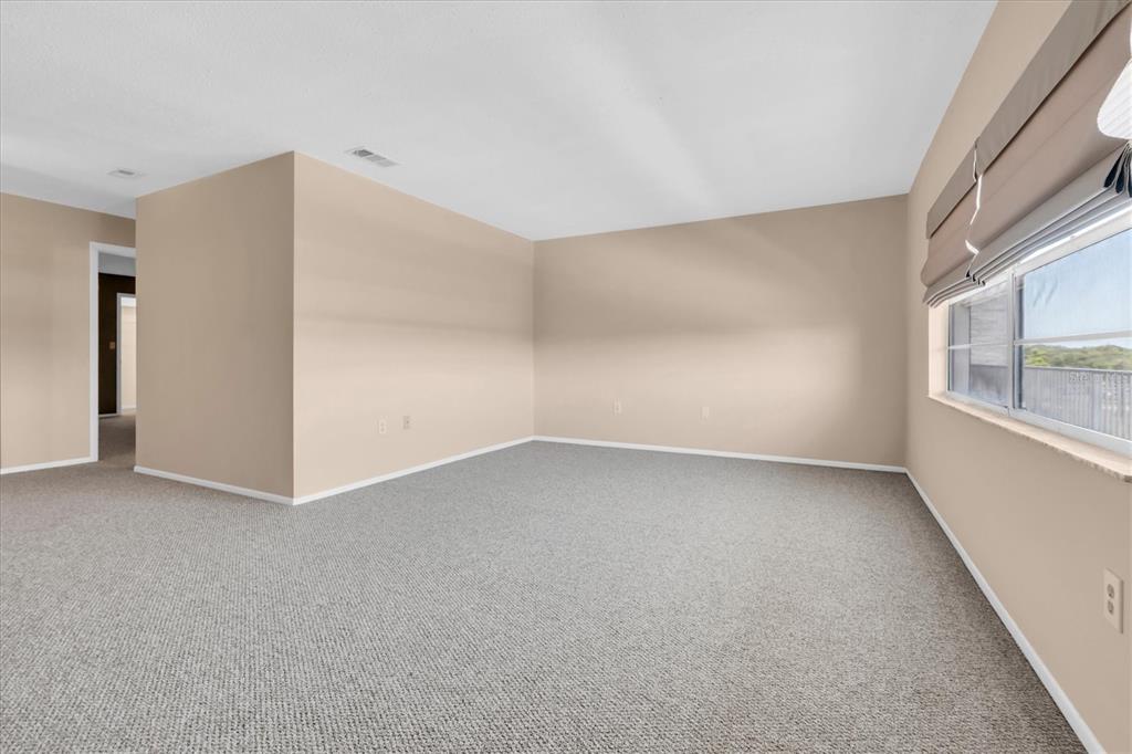 An empty room with beige walls, gray carpeting, and a large window with blinds — 5060 76TH AVENUE N UNIT 402, PINELLAS PARK, FL
