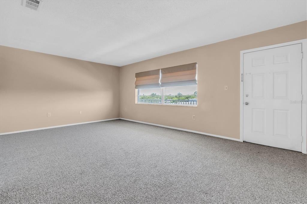 An empty room features beige walls, gray carpeting, a window with shades, and a white door — 5060 76TH AVENUE N UNIT 402, PINELLAS PARK, FL