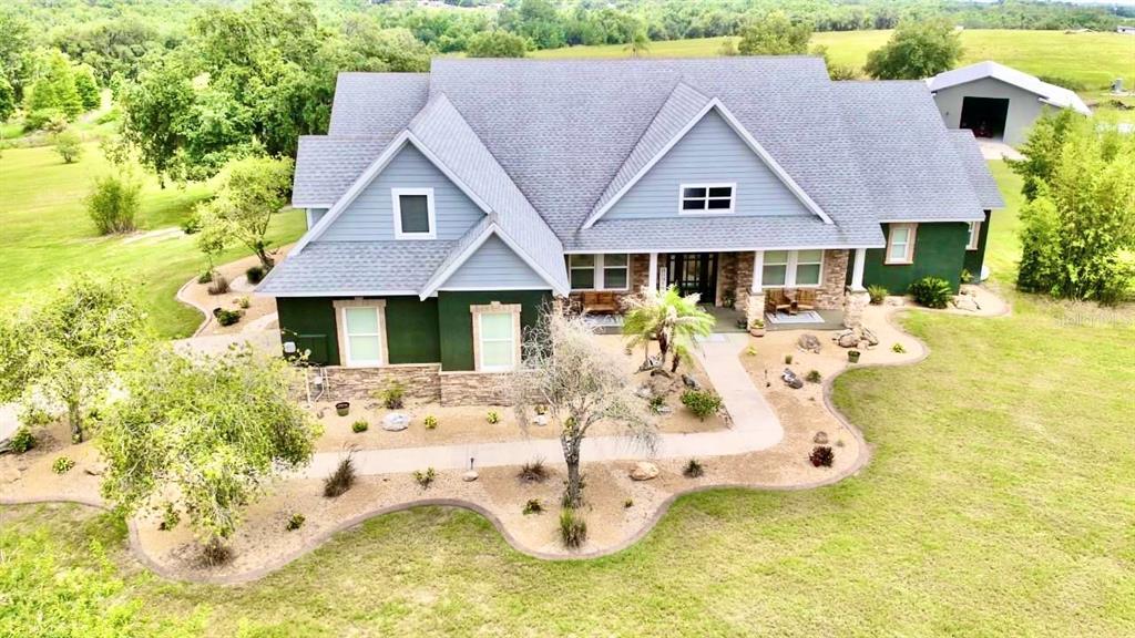 An aerial view of a two-story house with blue siding, stone accents, and a detached garage — 32112 JACK RUSSELL COURT, DADE CITY, FL