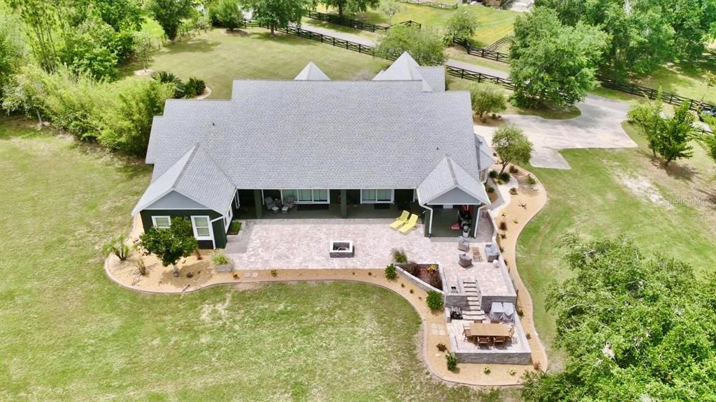 An aerial view of a house with a large stone patio, fire pit, and outdoor dining — 32112 JACK RUSSELL COURT, DADE CITY, FL