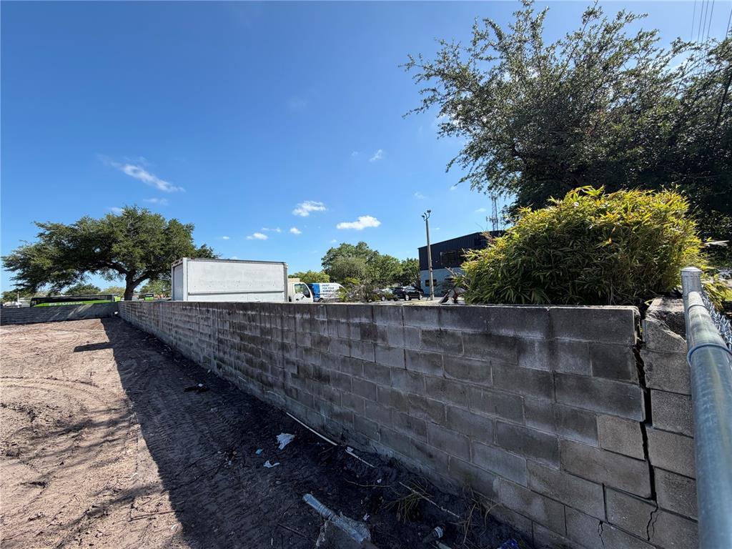 A concrete block wall runs along a dirt lot with trees and vehicles in the background — 503 N JOHN YOUNG PARKWAY, ORLANDO, FL