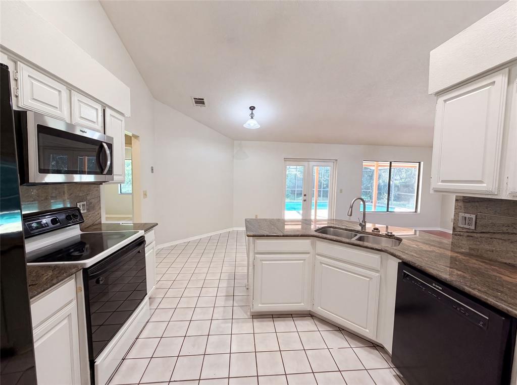A kitchen features white cabinets, granite countertops, black appliances, and white tile flooring — 332 SPRUCEWOOD ROAD, LAKE MARY, FL