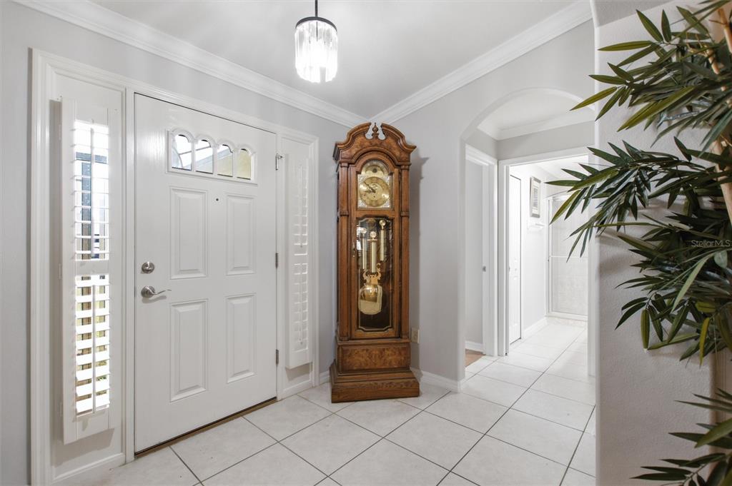 A white-tiled entryway features a wooden grandfather clock, a white front door, and a chandelier — 16416 SW 15TH COURT, OCALA, FL