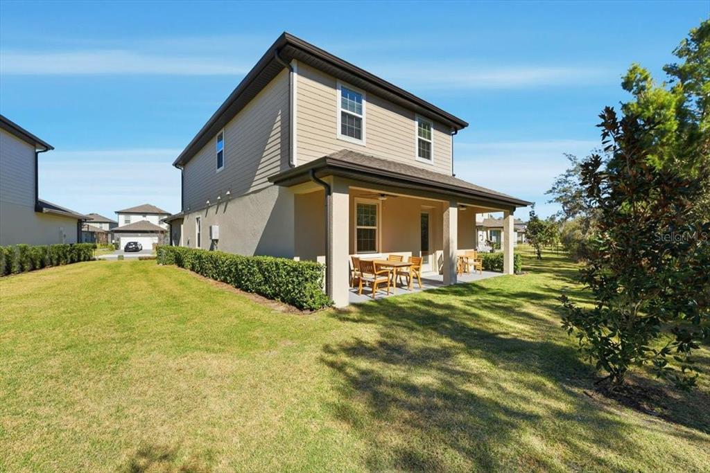 The exterior of a two-story house features a covered patio and a grassy backyard — 7792 SOMERSWORTH DRIVE, KISSIMMEE, FL