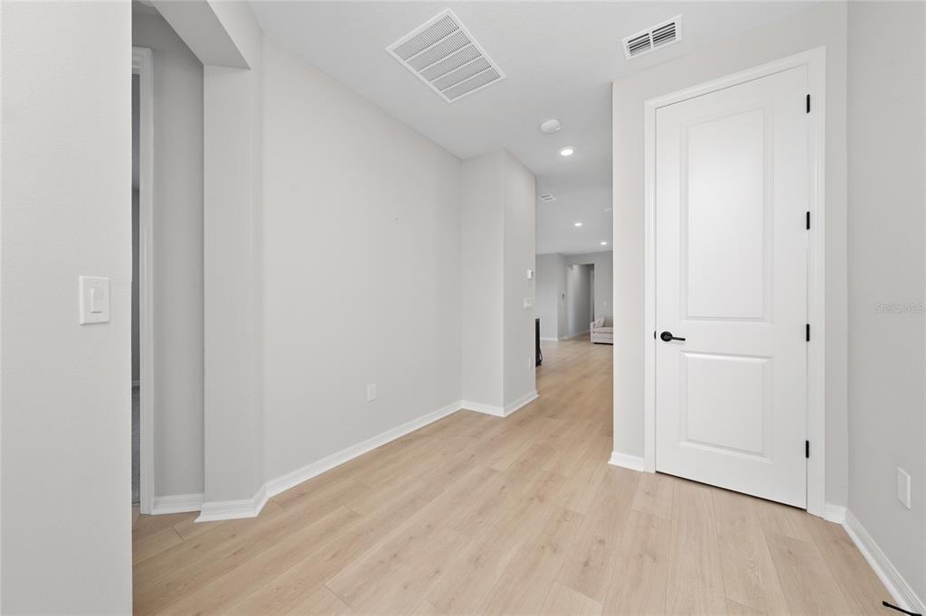 A hallway with light wood-look flooring, white walls, and a closed white door — 2914 SAILHOUSE DRIVE, ST CLOUD, FL