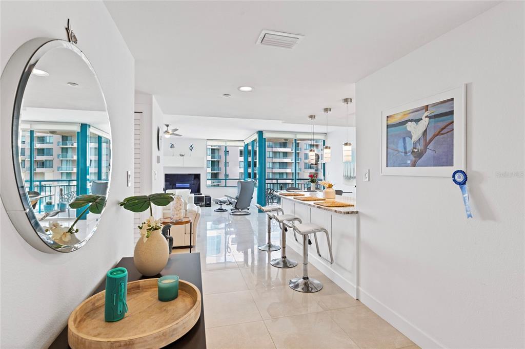 A bright, open-concept living area features a kitchen island with bar stools and tile flooring — 1520 GULF BOULEVARD UNIT 1807, CLEARWATER BEACH, FL