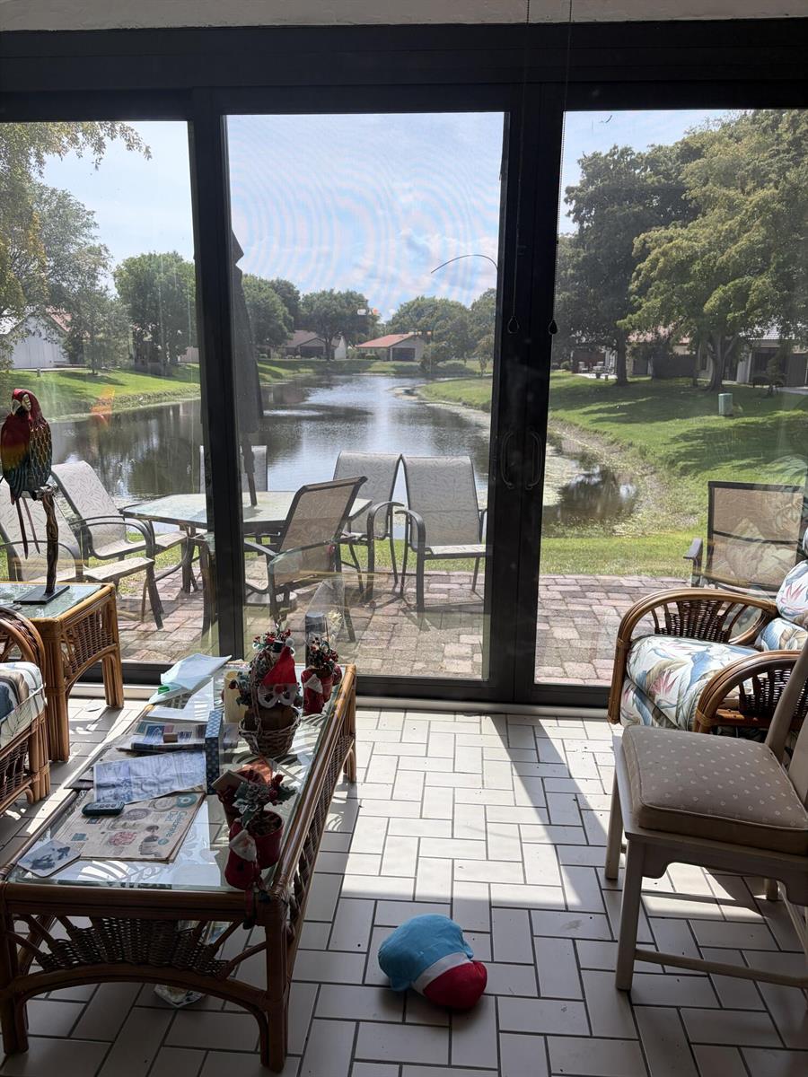 A sunroom with tile flooring and wicker furniture overlooks a backyard pond and patio area — 4807 Boxwood Circle, Boynton Beach FL 33436, BOYNTON BEACH, FL