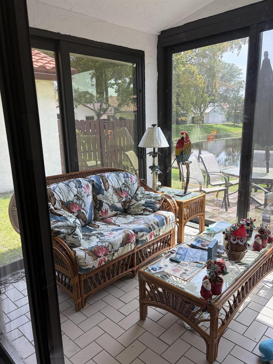 A sunroom features wicker furniture, floral cushions, a parrot statue, and views of a pond — 4807 Boxwood Circle, Boynton Beach FL 33436, BOYNTON BEACH, FL