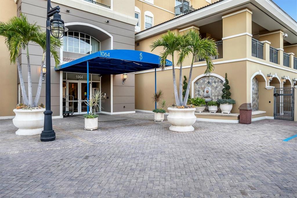 The exterior entrance of a building features a blue awning, palm trees, and stone planters — 1064 N TAMIAMI TRAIL UNIT 1527, SARASOTA, FL
