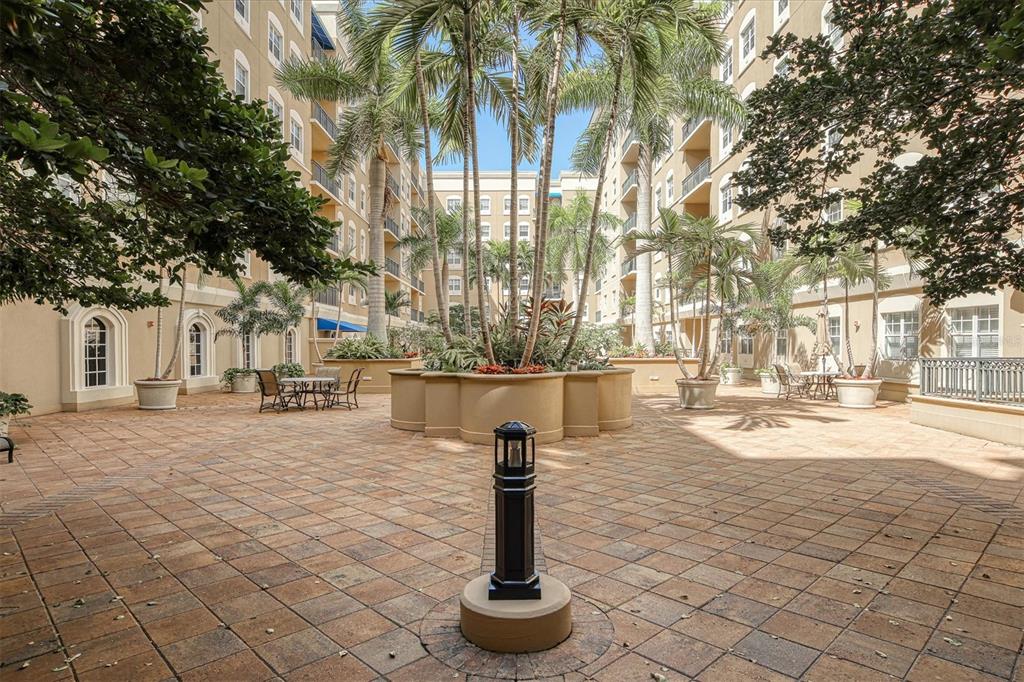 An outdoor courtyard features paved ground, palm trees, a central planter, and surrounding apartment buildings — 1064 N TAMIAMI TRAIL UNIT 1527, SARASOTA, FL