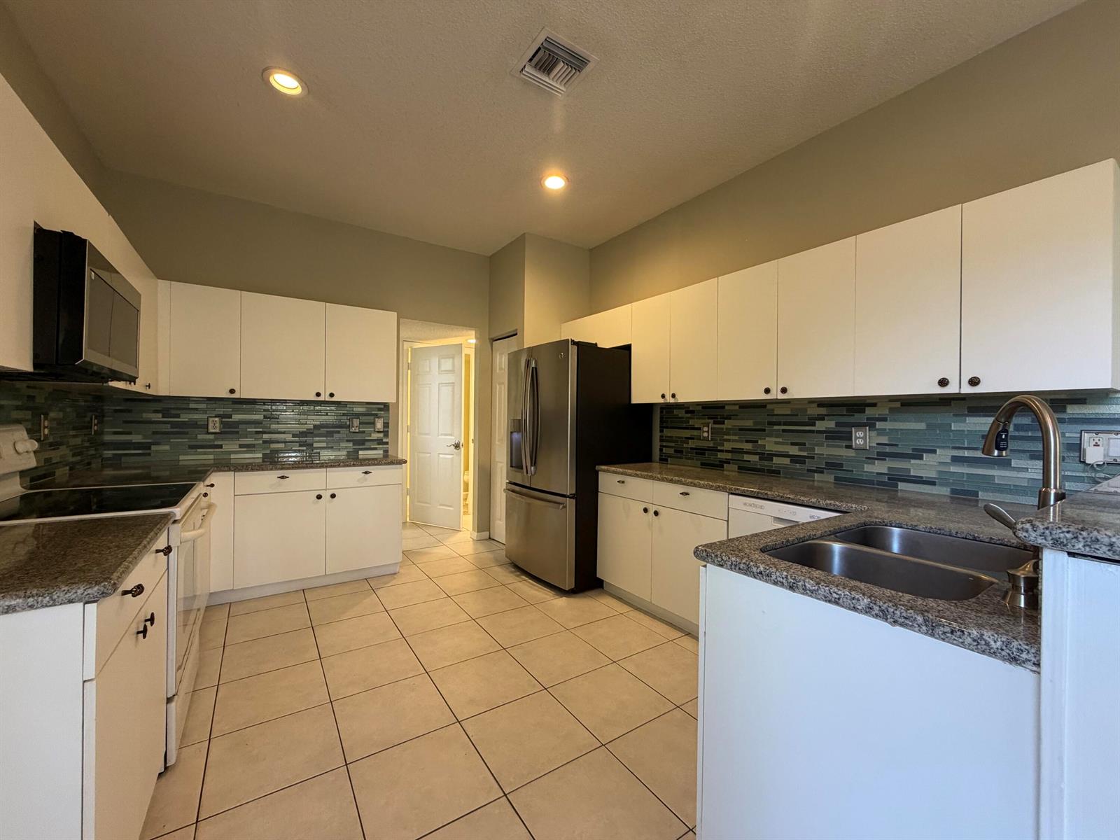 A kitchen features white cabinets, granite countertops, a stainless steel refrigerator, and a blue backsplash — 1848 Capeside, Wellington FL 33414, WELLINGTON, FL